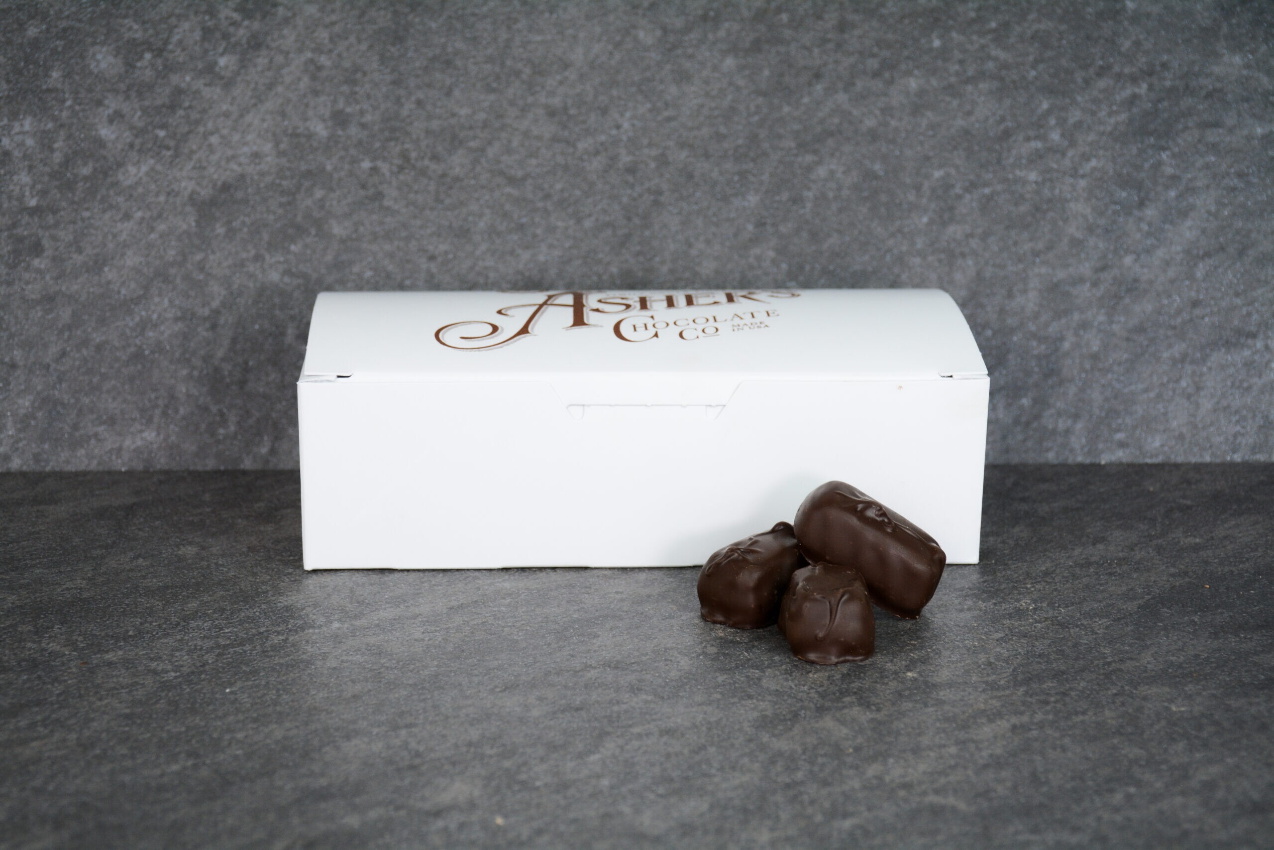 Dark chocolate covered jellies with raspberry filling displayed in front of a small white box