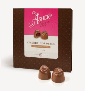 Milk Chocolate Cherry Cordials Traditional Box with pink and white Asher's Chocolate Co. Label. Two (2) cordials on the front of the box reveal, color, size, shape, and texture of candies. Two (2) Milk Chocolate Cherry Cordials sit outside of the box to reveal size, color, and chocolate texture. Displayed on white background.