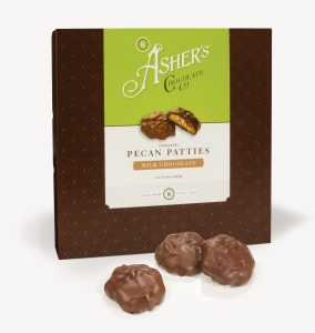 Milk Chocolate Caramel Pecan Patties Traditional Box with green and white Asher's Chocolate Co. Label. Two (2) Patties on the front of the box reveal, color, size, shape, and texture of candies. Three (3) Milk Chocolate Caramel Pecan Patties sit outside of the box to reveal size, color, and chocolate texture. Displayed on white background.