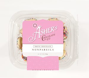 White Chocolate Nonpareils Fresh Pack with pink and white Asher's Chocolate Co. Label. Clear Fresh Pack shows white chocolate drops covered in rainbow seeds.
