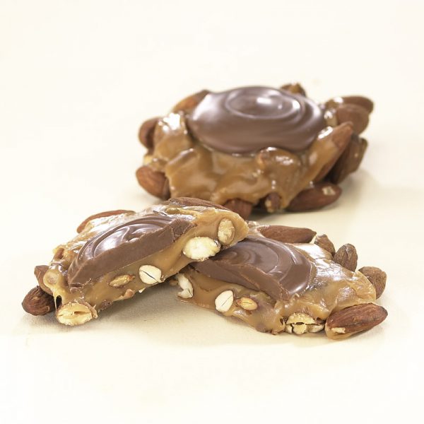 Almond Praline Hand Crafted Milk Chocolate shown on white background. One (1) praline is shown cut in half, to reveal the chocolate topping, nuts, and caramel filling. One(1) praline is shown whole in the background.