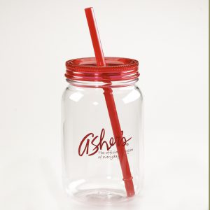 Clear Cold Beverage Cup with Asher's Logo in red script is written with 'The official chocolate of everyday life.' slogan. A red straw is in the mason jar shaped tumbler. It sits on a white background.