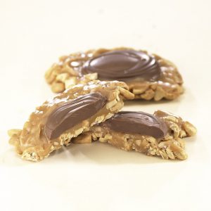 Cashew Praline Hand Crafted Milk Chocolate shown on white background. One (1) praline is shown cut in half, to reveal the chocolate topping, nuts, and caramel filling. One(1) praline is shown whole in the background.