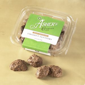 Milk Chocolate Coconut Clusters clear Fresh Pack with green and white Asher's Chocolate Co. Label. Four (4) Milk Chocolate Coconut Clusters are outside of the Fresh pack to reveal size, color, filling, and texture.