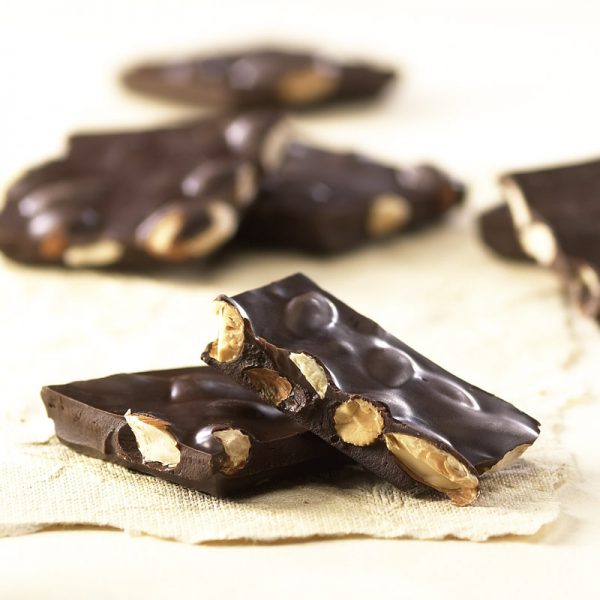 Dark Chocolate Almond Bark pieces on tan sheet. Large, thick pieces reveal chunks of almonds covered in dark chocolate.