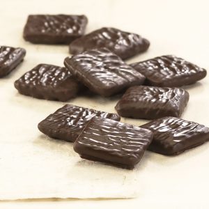 Dark Chocolate Mini Grahams scattered on white background revealing size, shape, texture, and dark chocolate coating.