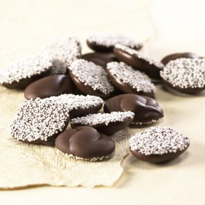 Milk Chocolate Nonpareils. Drops are scattered on tan sheet to reveal size, color, and texture. White seeds coat one side of the drop.