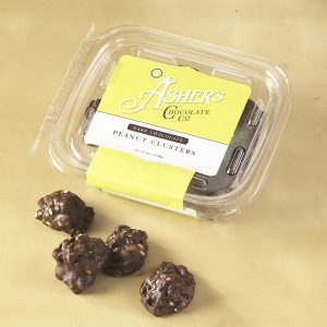 Dark Chocolate Peanut Clusters Fresh Pack with yellow and white Asher's label. Four (4) Dark Chocolate Peanut Clusters are outside of the Fresh pack to reveal size, color, filling, and texture.