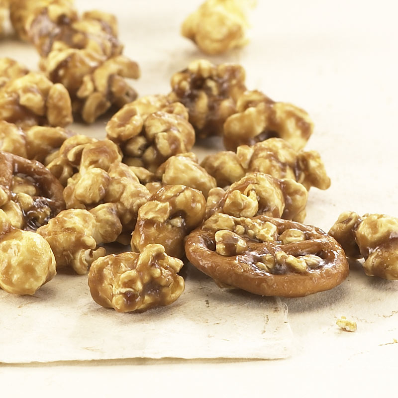 Keystone Crunch scattered on tan background to reveal pinwheel pretzels, caramel coated popcorn, and toffee nuts.
