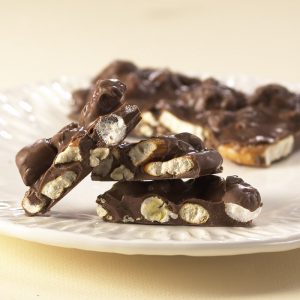 Milk Chocolate Boardwalk Crunch chunks lie on white plate to reveal the chocolate toppings.