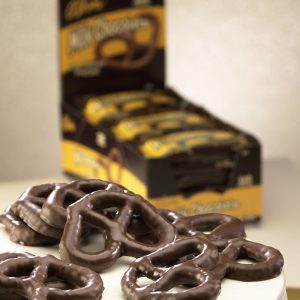 Milk Chocolate Covered Pretzel with Caddy in the background. Milk Chocolate Pretzels lie on a pile of pretzels.