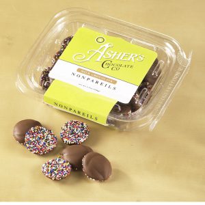 Milk Chocolate Nonpareils clear Fresh Pack with yellow and white Asher's Chocolate Co. Label. Six (6) milk chocolate drops are scattered outside of Fresh Pack to reveal size, color, and texture.