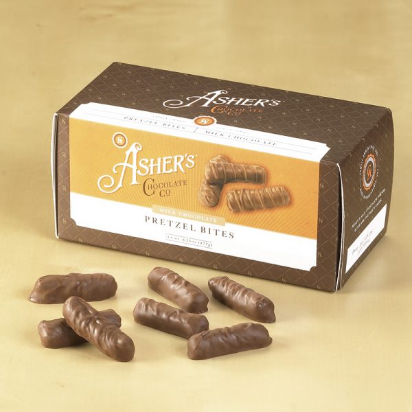 Milk Chocolate Pretzel Bites Snack Box with brown, white, and orange design. Milk Chocolate Pretzel Bites scattered in front of white backdrop, revealing candies shape, size, and chocolate texture.