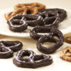 Dark Chocolate Covered Pretzels three (3) ring scattered on white plate. Size, shape, and texture are shown compared to non-chocolate coated pretzels in the background.