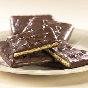Milk Chocolate Graham Crackers lie on a pile of Grahams on white plate. The two (2) focal grahams are broken open to reveal the golden graham inside.