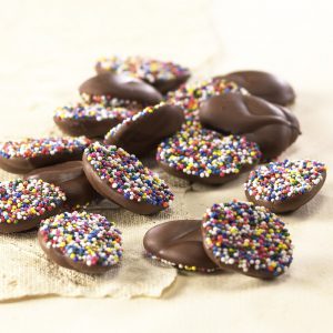 Milk Chocolate Nonpareils scattered on tan background with rainbow seeds.