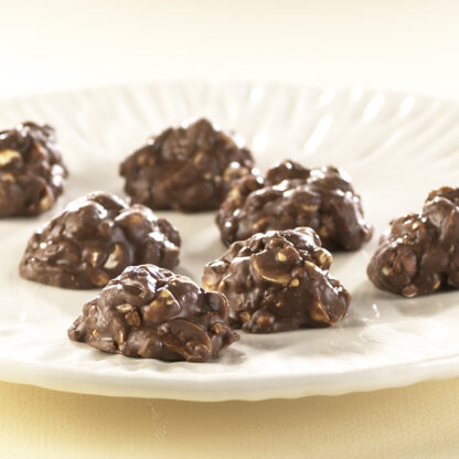 Milk Chocolate Peanut Clusters on white plate. Milk Chocolate chunks are sitting to reveal peanuts coated in globs of milk chocolate.