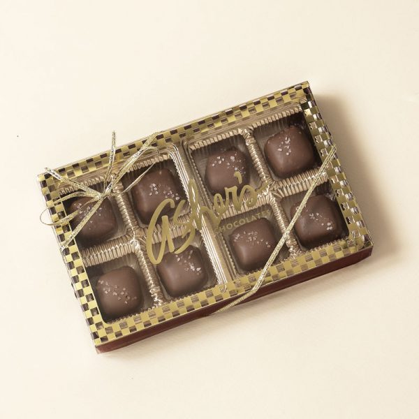 Sea Salt Caramel Asher's Chocolate gift box with clear lid and gold checkered trim reveals eight (8) Sea Salt Caramels inside. A thin gold bow wraps the box. Pictured on white background.