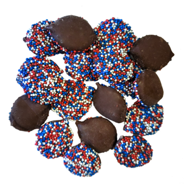 Milk Chocolate Nonpareils. Drops are scattered on tan sheet to reveal size, color, and texture. White seeds coat one side of the drop.