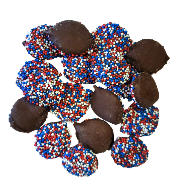 Milk Chocolate Nonpareils. Drops are scattered on tan sheet to reveal size, color, and texture. White seeds coat one side of the drop.