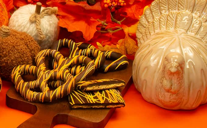 Close-up of Thanksgiving-themed candy against orange backdrop, including chocolate-covered pretzels, pumpkins, turkey decor