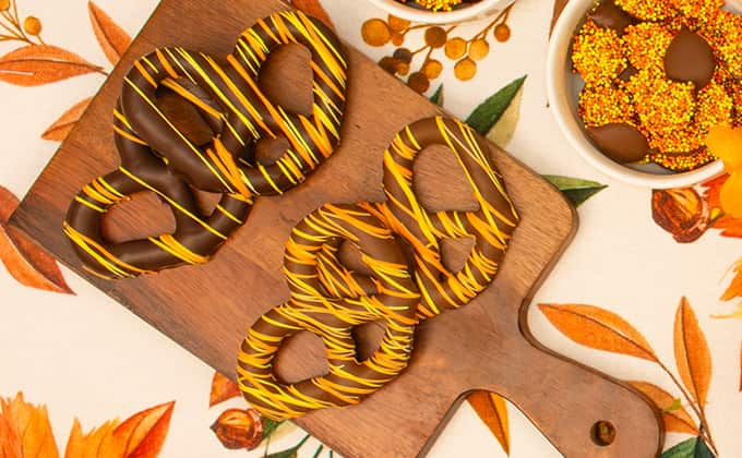 Close-up of Thanksgiving-themed candy against white backdrop, including chocolate-covered pretzels, nonpareils, and leaves