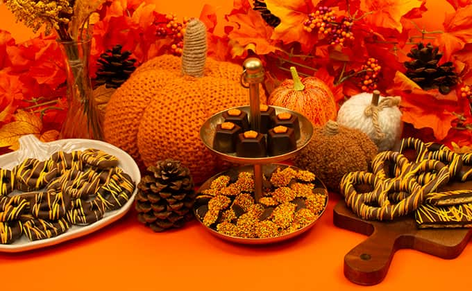 Fall scene of orange background, leaves, and pumpkins on a table with a spread of chocolates and candy