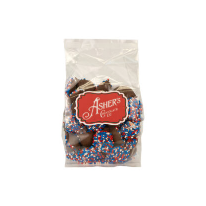 A clear bag of “America 250” Nonpareils LIMITED EDITION - Red/White/Blue, chocolate candies coated in red, white, and blue sprinkles, featuring a red Ashers Chocolate Co. label on the front.