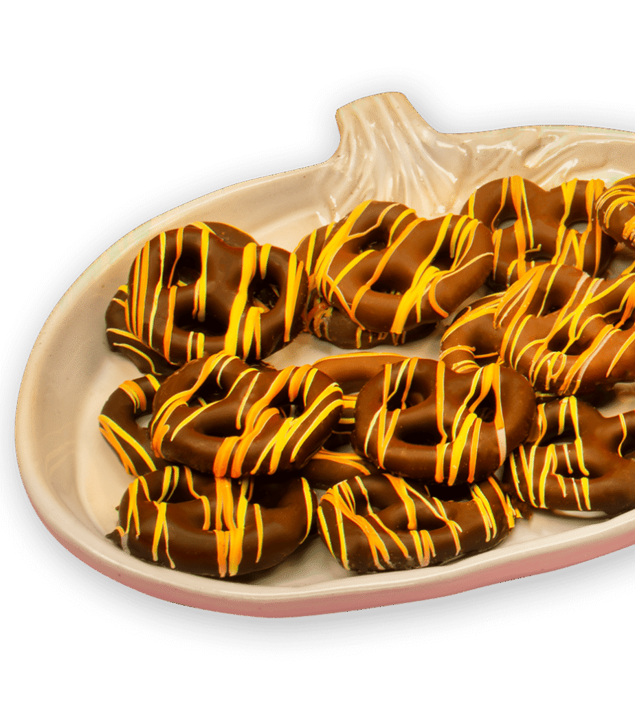 A ceramic pumpkin-shaped tray holds chocolate-covered pretzels drizzled with orange and yellow icing.