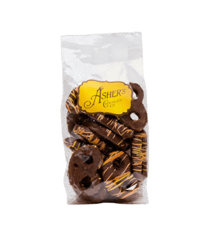A clear bag of chocolate-covered pretzels with yellow drizzle, labeled Ashers Chocolate Co. on a yellow tag, set against a white background.