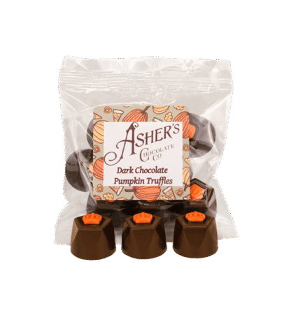 A clear bag labeled Ashers Dark Chocolate Pumpkin Truffles contains round chocolates with orange pumpkin decorations. Four truffles are displayed in front of the bag.