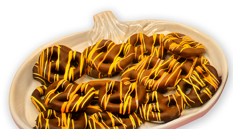 Chocolate-covered pretzels with orange and yellow drizzle are arranged on a pumpkin-shaped plate.