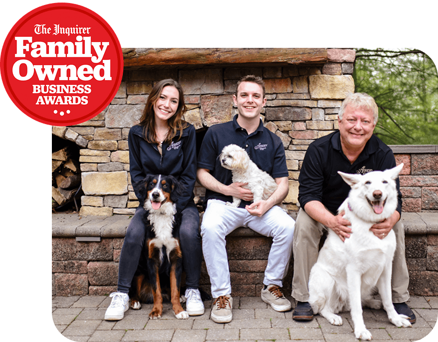 Asher family sitting on a stone wall, each holding a dog, with a The Inquirer Family Owned Business Awards badge in the corner.