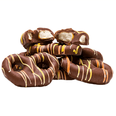 A pile of chocolate-covered pretzels drizzled with orange and yellow icing, with two broken pieces showing the crunchy interior.