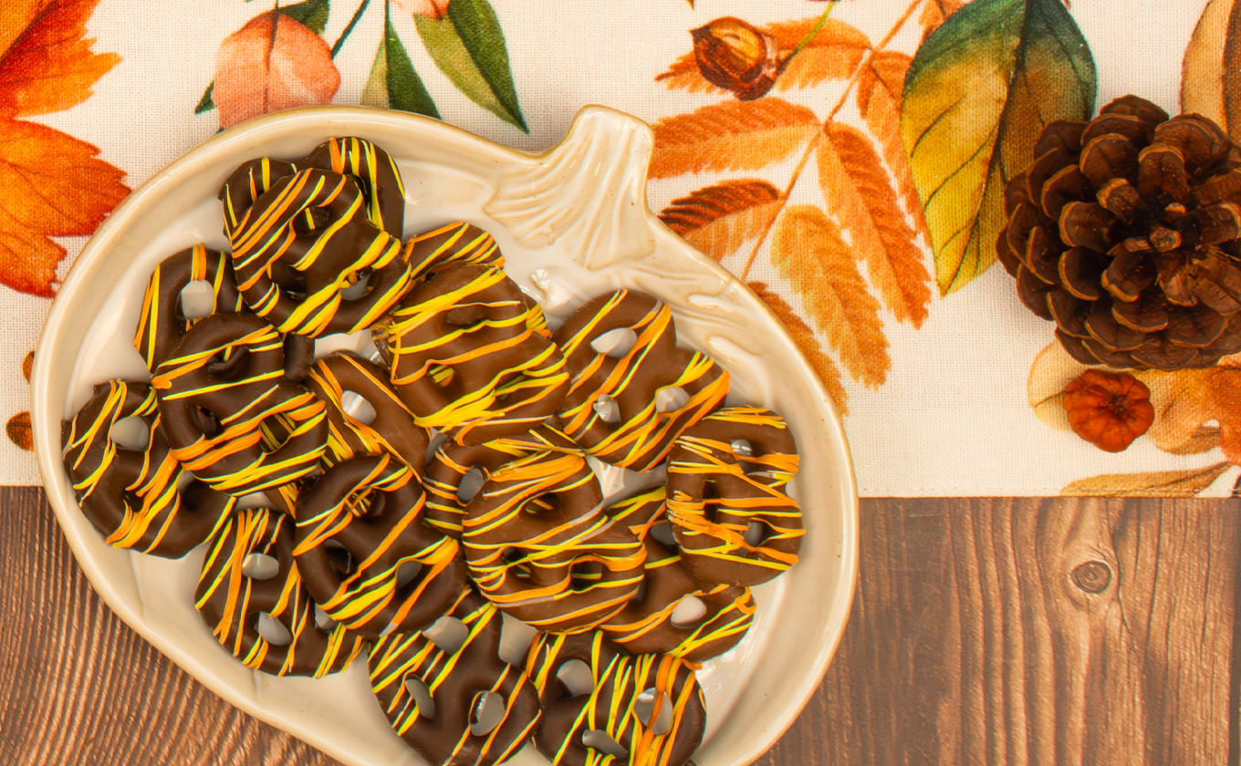 Chocolate-covered pretzels drizzled with yellow and orange icing on a pumpkin-shaped platter.